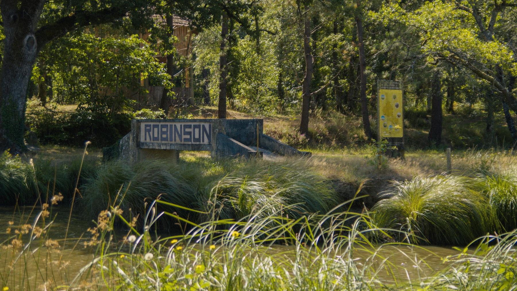 Un ponton de béton marqué Robinson au bord d'un plan d'eau, dans la verdure.