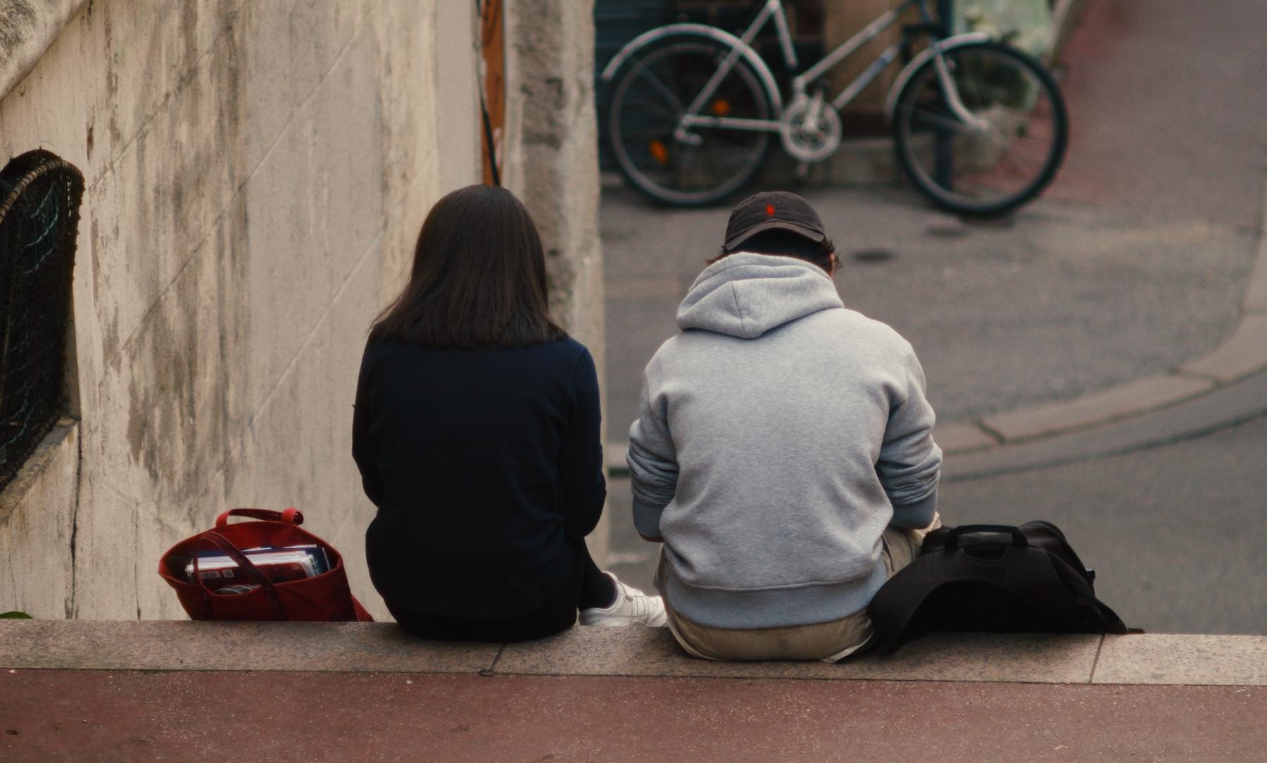 Un couple assis de dos en haut d'un escalier, un vélo blanc en contrebas.