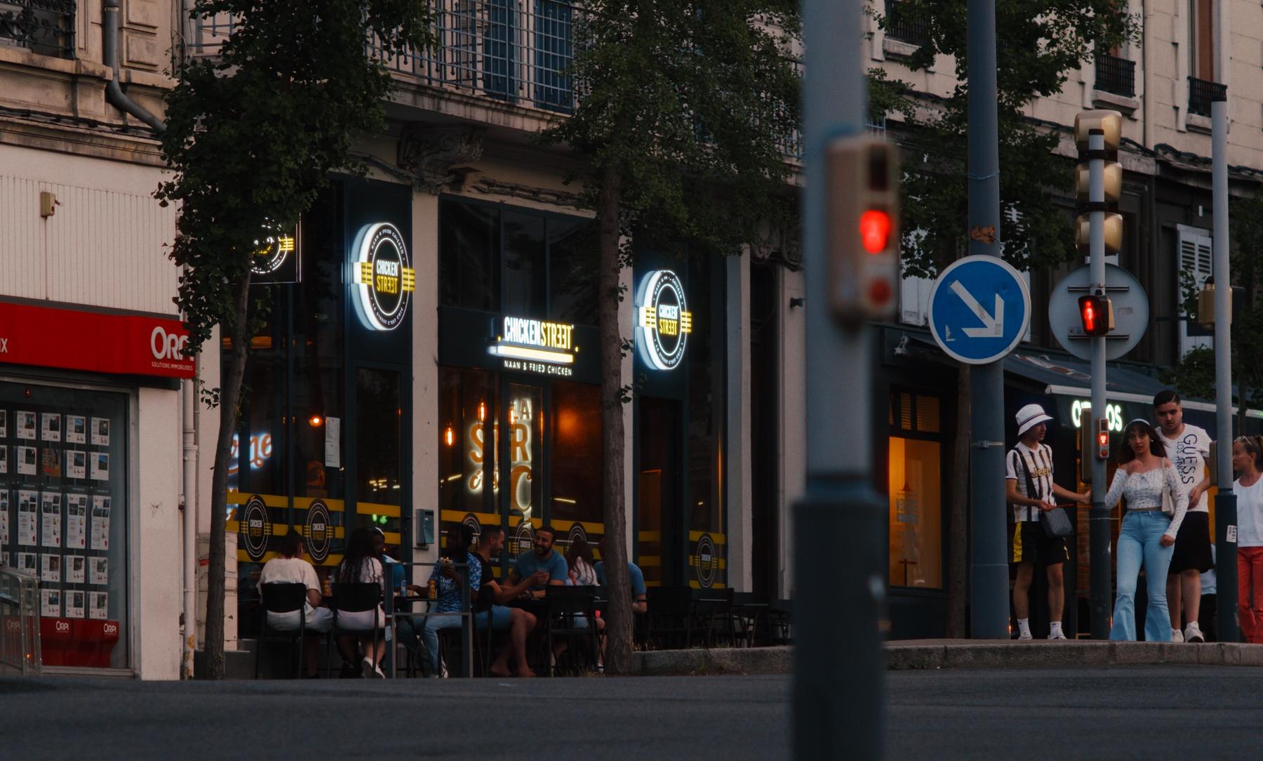 Une terrasse de fast-food au soir, enseignes allumées.