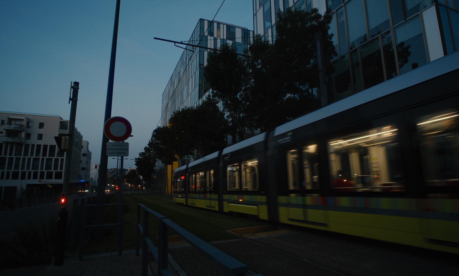 Le tramway jaune passe de nuit devant les façades de verre.