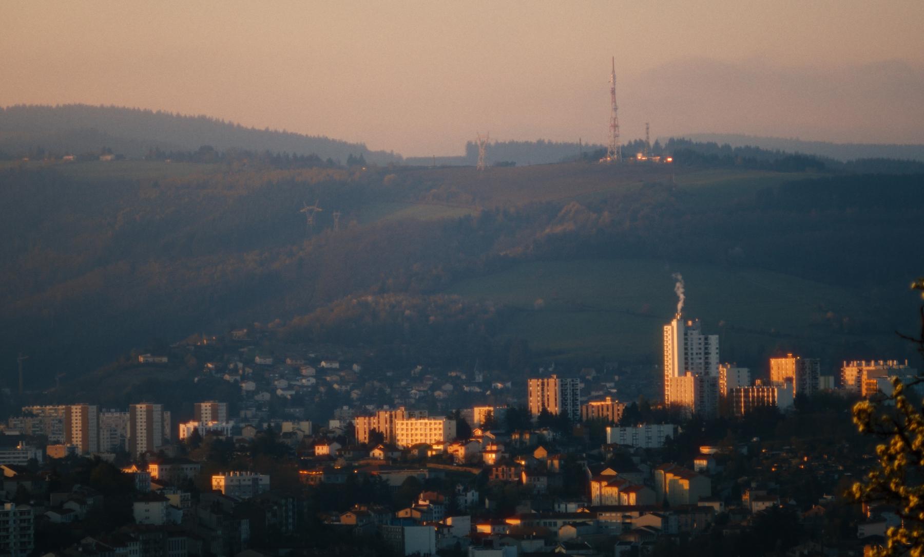 La ville au soleil couchant, tours et collines dans une lumière dorée.